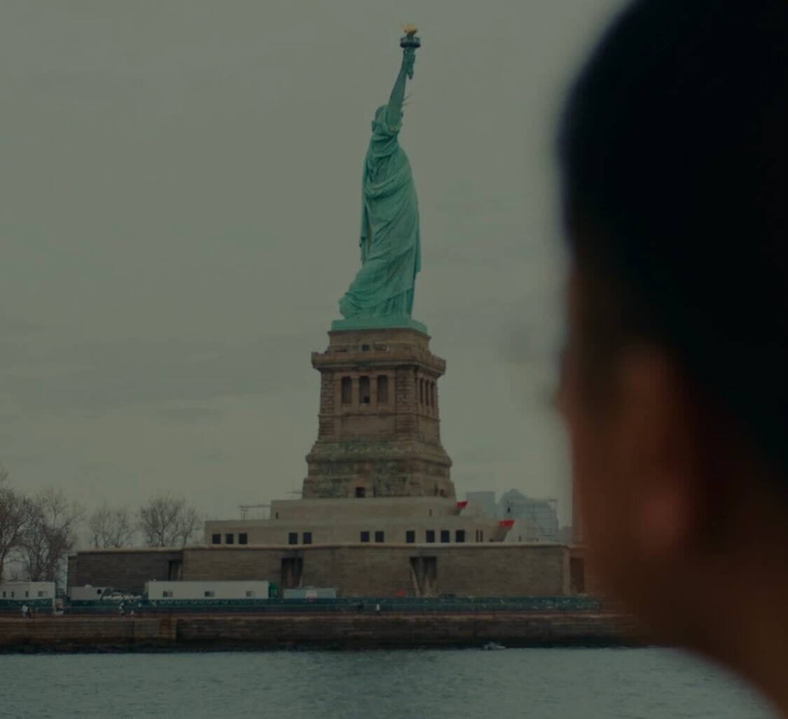 A young man, seen from behind, looks across the water at the Statue of Liberty.